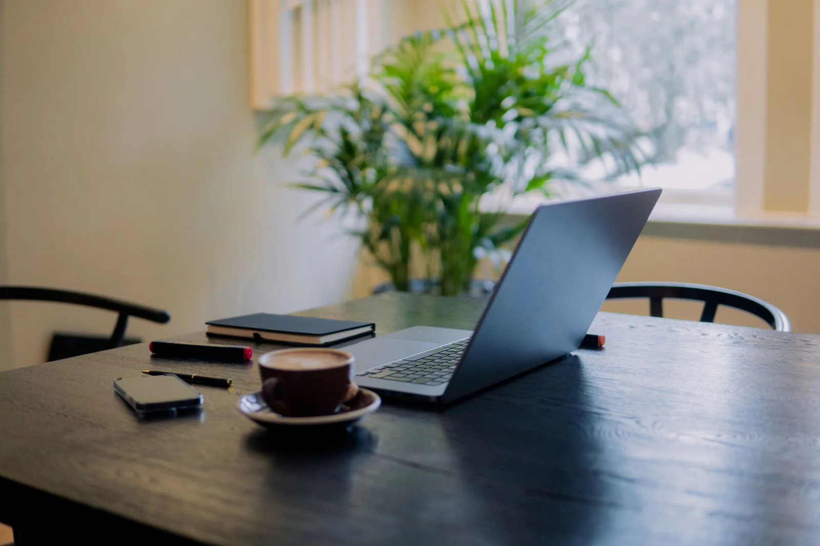 Un bureau de freelance avec un ordinateur portable et un carnet, éclairé par la lumière du matin