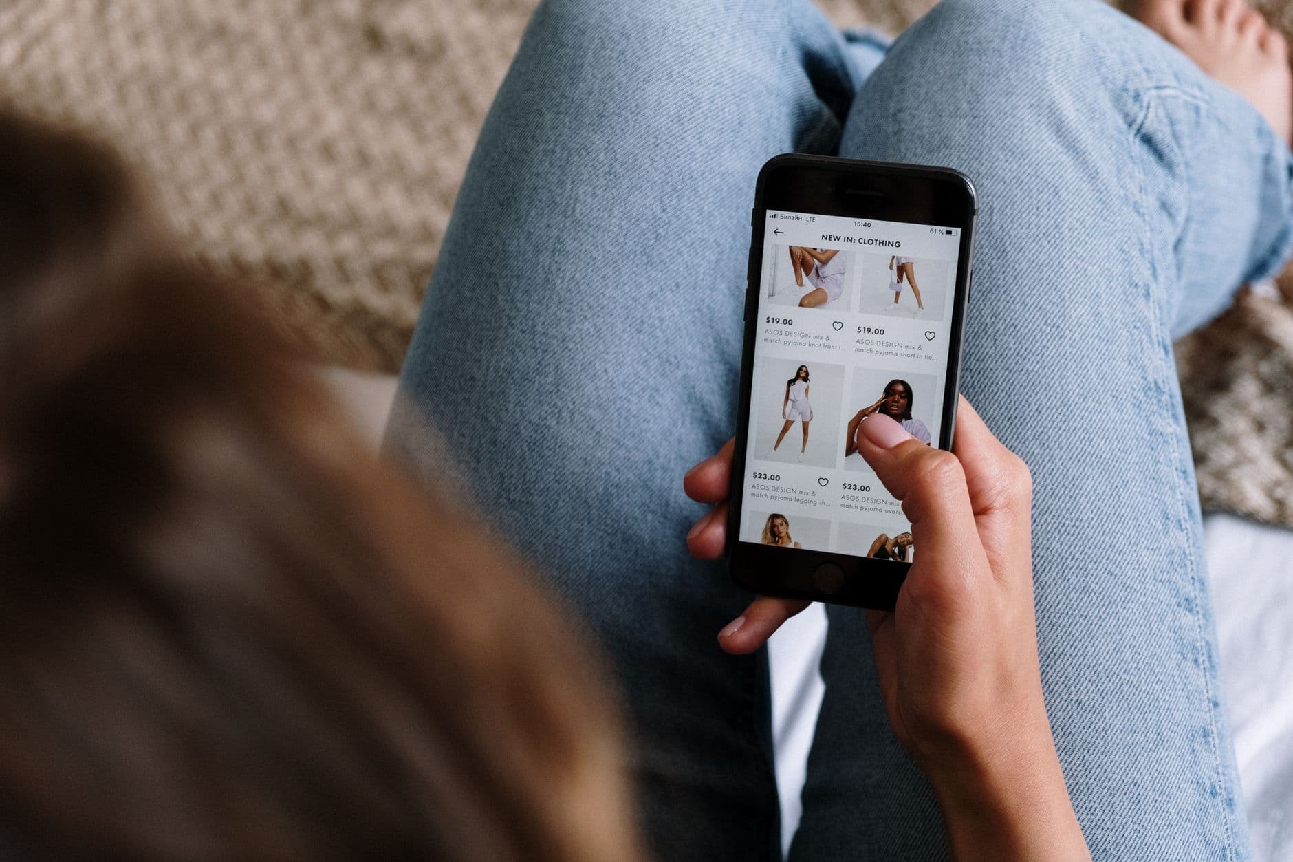 Téléphone posé sur une surface en bois clair, écran affichant une application de vente de vêtements, lumière naturelle douce